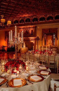 a table set up for a formal dinner with gold plates and red flowers on it