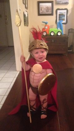 a small child dressed up as a roman gladia with a spear and shield in his hands