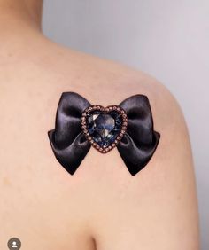 the back of a woman's shoulder with a bow and heart tattoo on it