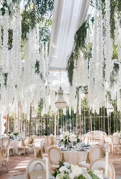 an outdoor wedding reception with white flowers hanging from the ceiling and chandeliers in the background