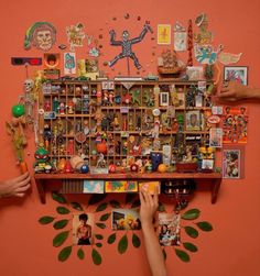 two hands are reaching for pictures on the wall above a shelf with many different items