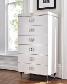 a white chest of drawers sitting on top of a hard wood floor next to a window