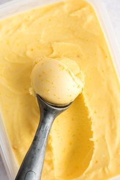 a scoop of ice cream in a container with a metal spoon on the top and yellow liquid behind it