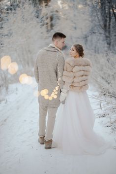 a bride and groom standing in the snow with their fur coat over their shoulders, looking at each other