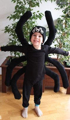 a young boy in a black spider costume standing on the floor with his arms up