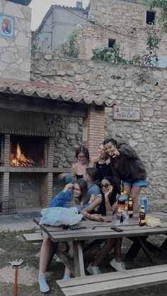 a group of people sitting at a picnic table in front of an open fire place