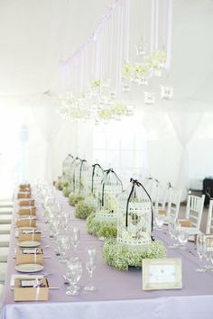 the table is set up with white flowers and birdcages on it, along with empty wine glasses