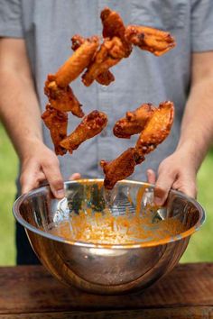 a person holding a metal bowl filled with chicken wings