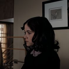 a woman standing in front of a window next to a framed photo on the wall