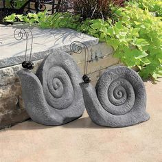 two stone snail sculptures sitting on top of a cement slab next to a planter