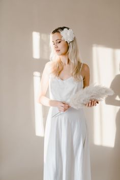 a woman wearing a white dress and feather headpiece standing in front of a window