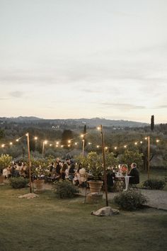 an outdoor dinner is set up in the middle of a field with string lights strung over it