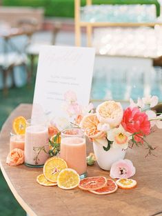 a table topped with oranges and drinks on top of a wooden table next to a sign