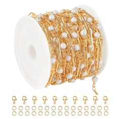 a spool of gold plated metal with white beads and chains attached to it