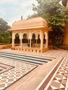 a gazebo in the middle of a pool surrounded by trees and bushes with tiled flooring