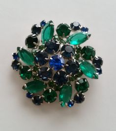 Brilliant Bright Blue And Green Silvery Pinwheel Flower Brooch Authentic Collectible Mid Century Luxury Vintage Costume Jewelry... This Bright Beautiful Pinwheel Flower Brooch is a Mid Century Delight for the Eyes. It's comprised of Sparkling Emerald Green and Sapphire Blue Crystal Rhinestones in both Round and Marquise shapes all prong set in a Shiny Silver tone finish. The Gorgeous color combination and Wonderful sense of movement this Pristine piece evokes make this a Delightfully Dazzling ad Pinwheel Flower, Juliana Jewelry, Designer Costume Jewelry, Vintage Lover, Shiny Silver, Green Crystals, Vintage Costume Jewelry, Glass Necklace, Flower Brooch