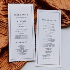 two white wedding program cards sitting on top of a brown cloth covered tablecloth next to each other