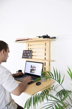 a man sitting in front of a laptop computer on top of a wooden desk next to a potted plant