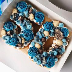 two decorated cookies in a box with blue icing and decorations on the top one