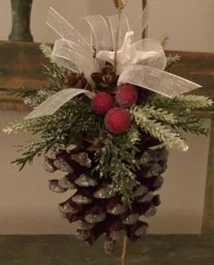 a pine cone with berries and greenery in it sitting on a table next to a vase