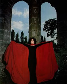 a woman with a red cape standing in front of an old building