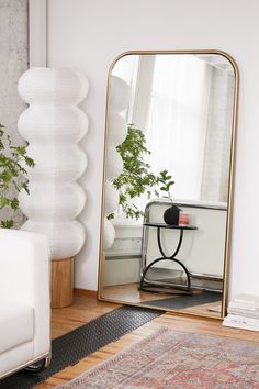 a large mirror sitting on top of a wooden floor next to a white couch and table