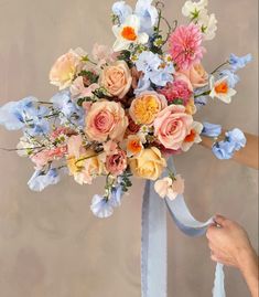 a bouquet of flowers is being held up by someone's hand with a blue ribbon