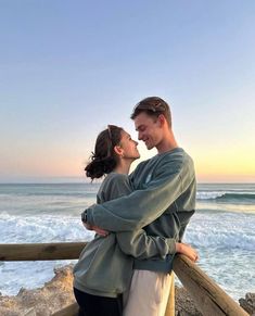 a man and woman standing next to each other near the ocean with waves in the background