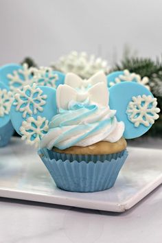 cupcakes decorated with blue and white frosting are on a tray next to pine branches