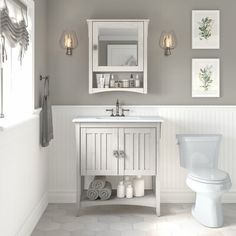 a white toilet sitting next to a sink in a bathroom under two pictures on the wall