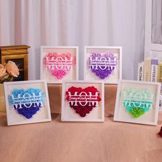 four framed paper hearts with the words mom in different colors and sizes are on a table