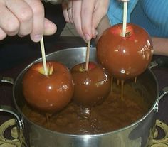 three chocolate covered apples being dipped with toothpicks in a metal pan on a table