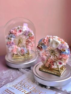 two glass globes with flowers in them on top of a table next to a book