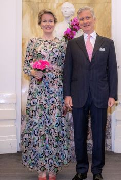 a man and woman standing next to each other in front of a wall with flowers