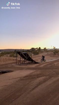 a man riding a bike down a dirt road next to a ramp on top of a hill