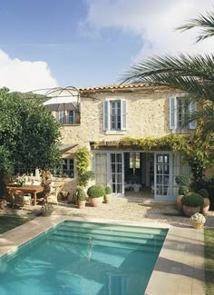 an outdoor swimming pool in front of a house with trees and shrubs around it,