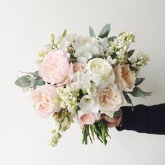 a person holding a bouquet of white and pink flowers with greenery in their hands