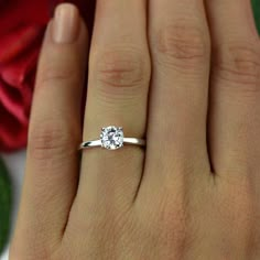 a woman's hand with a white diamond ring on her finger and red rose in the background