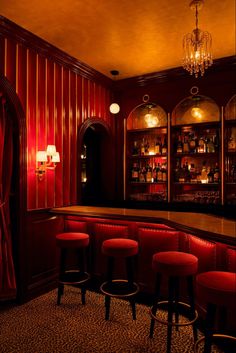 a dimly lit bar with red leather stools and chandelier hanging from the ceiling