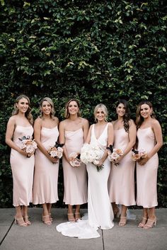 a group of women standing next to each other in front of a green wall holding bouquets