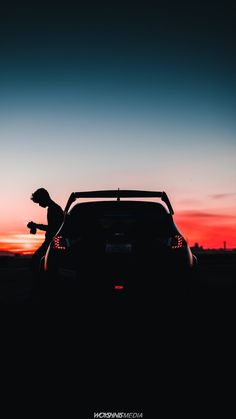 the silhouette of a person leaning against a car at sunset with their hand on the hood