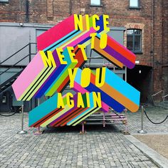 a colorful sculpture with words written on it in the middle of a brick walkway next to a building