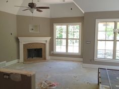 an empty living room with a fireplace and two windows in the middle of the room