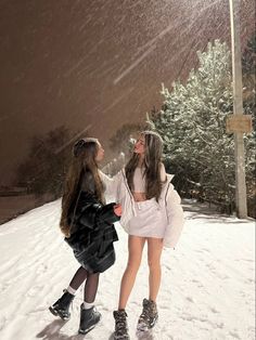 two girls are standing in the snow with their arms around each other as they look up into the sky