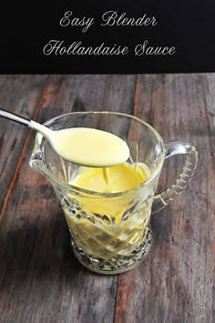 a glass cup filled with liquid on top of a wooden table next to a spoon