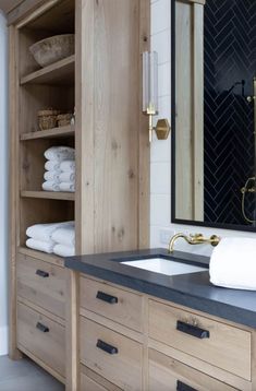 a bathroom with wooden cabinets and black counter tops, gold faucet, white towels