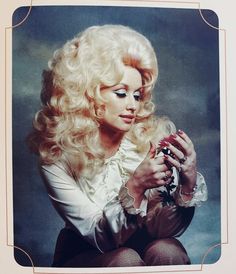 a woman with long blonde hair sitting on the ground and holding a flower in her hand