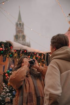 a woman taking a photo with her camera in front of a christmas tree and clock tower