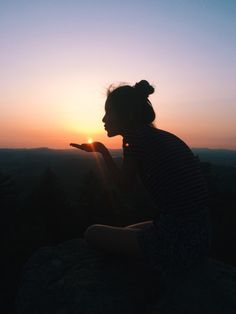 a woman sitting on top of a hill holding a cell phone in her hand at sunset