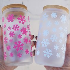 two hand painted mason jars with snowflakes on them, one is pink and the other is white